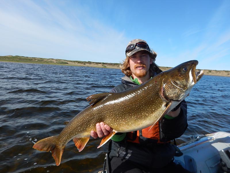 Scientist in small skiff on lake holding up captured lake trout